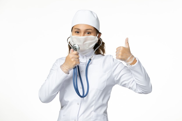 Vista frontal joven doctora con máscara protectora estéril debido al coronavirus con estetoscopio en el piso blanco
