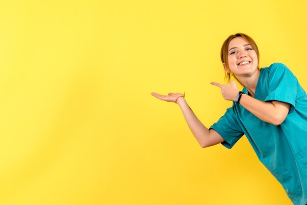 Vista frontal de la joven doctora sonriendo en la pared amarilla