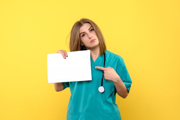 Vista frontal de la joven doctora sosteniendo archivos en la pared amarilla