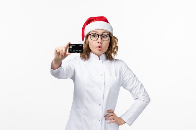 Vista frontal joven doctora sosteniendo una tarjeta bancaria en la pared blanca enfermera de vacaciones año nuevo