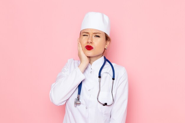 Vista frontal joven doctora en traje blanco con estetoscopio azul posando en el espacio rosa trabajo mujer niña emociones