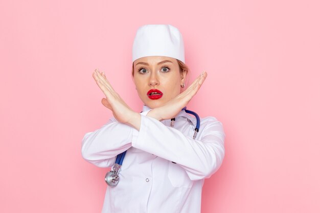 Vista frontal joven doctora en traje blanco con estetoscopio azul posando con gesto de prohibición en el médico de hospital de medicina de trabajo espacial rosa