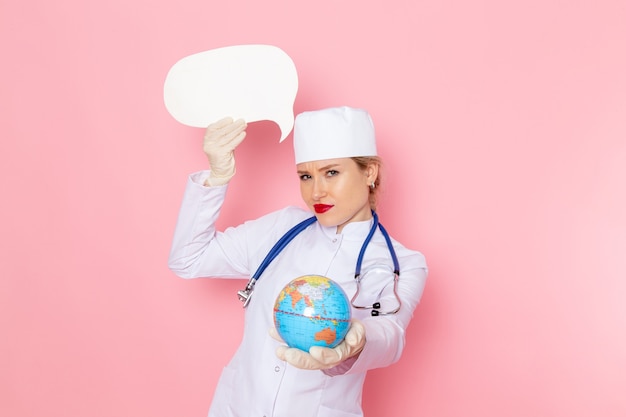 Foto gratuita vista frontal joven doctora en traje médico blanco con estetoscopio azul con globo y cartel blanco en la salud del hospital médico de medicina espacial rosa