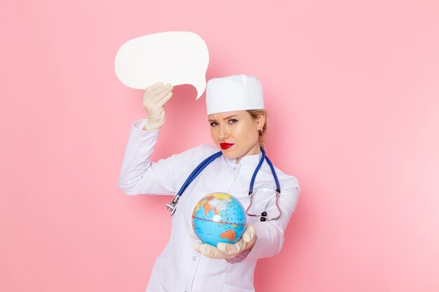 Vista frontal joven doctora en traje médico blanco con estetoscopio azul con globo y cartel blanco en la salud del hospital médico de medicina espacial rosa