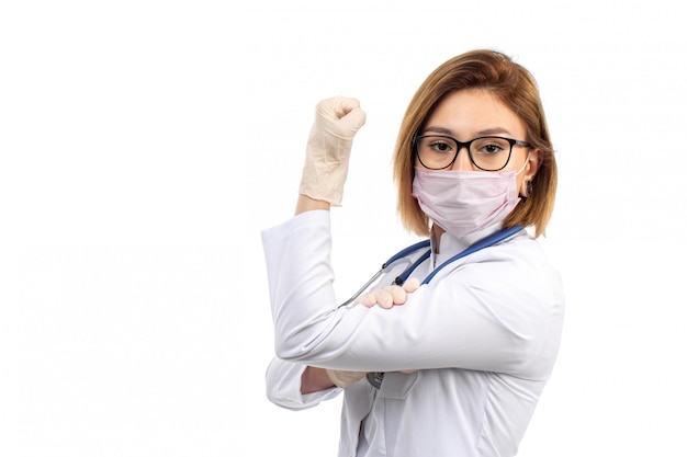 Foto gratuita una vista frontal joven doctora en traje médico blanco con estetoscopio con máscara protectora blanca con guantes en el blanco