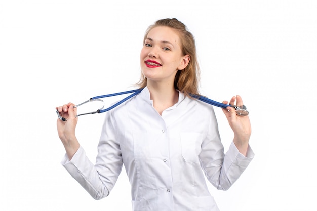 Una vista frontal joven doctora en traje médico blanco con estetoscopio sonriendo en el blanco