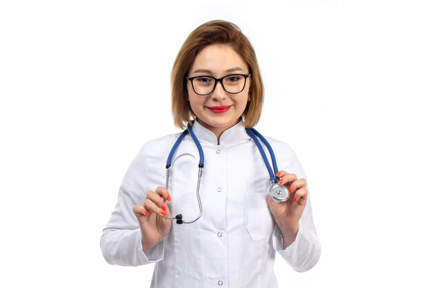 Una vista frontal joven doctora en traje médico blanco con estetoscopio sonriendo en el blanco