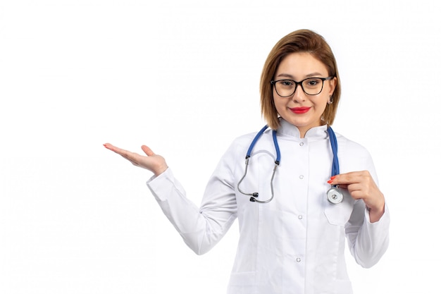 Una vista frontal joven doctora en traje médico blanco con estetoscopio sonriendo en el blanco