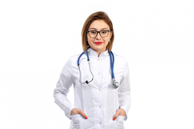 Una vista frontal joven doctora en traje médico blanco con estetoscopio sonriendo en el blanco