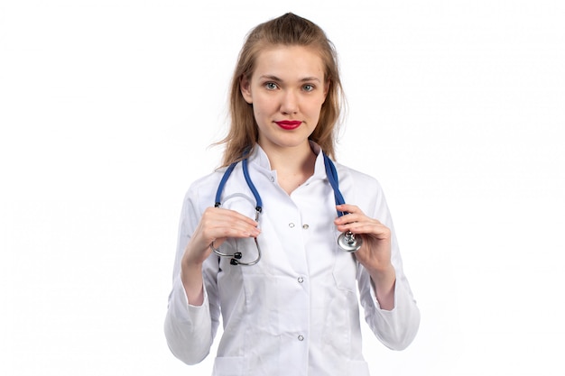 Una vista frontal joven doctora en traje médico blanco con estetoscopio sonriendo en el blanco