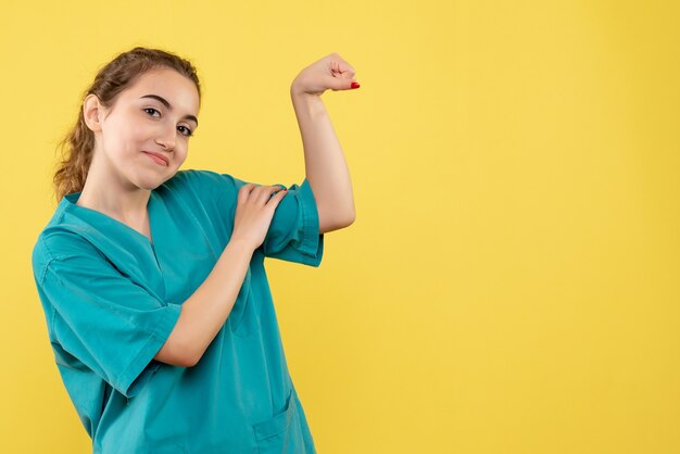 Vista frontal de la joven doctora en traje médico en la pared amarilla