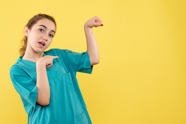 Vista frontal de la joven doctora en traje médico en la pared amarilla