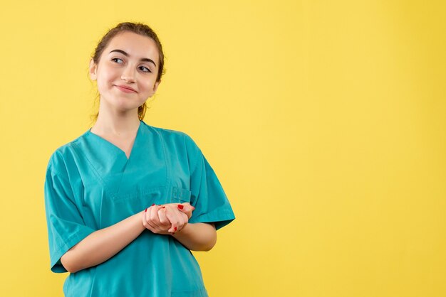 Vista frontal de la joven doctora en traje médico en la pared amarilla
