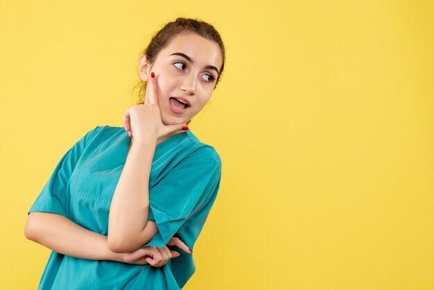 Vista frontal joven doctora en traje médico posando sobre fondo amarillo