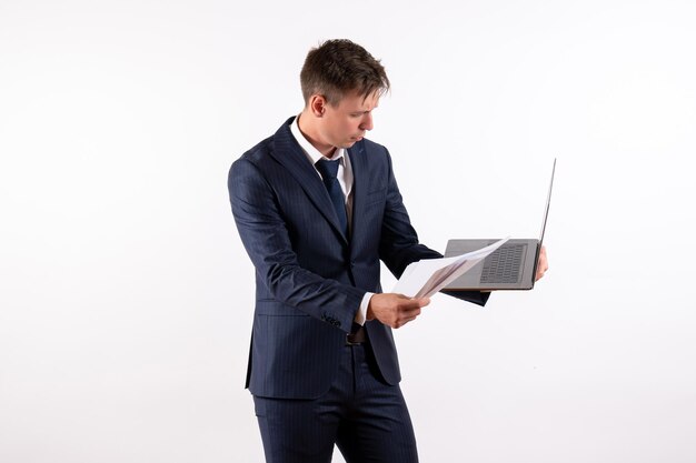 Vista frontal joven en elegante traje clásico usando su computadora portátil sobre fondo blanco.