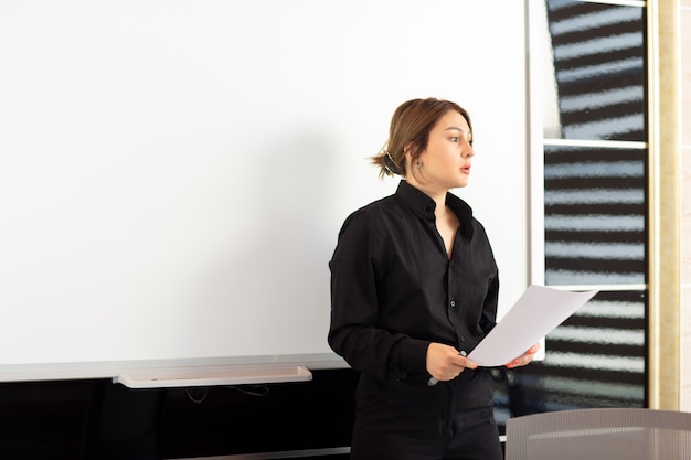 Una vista frontal joven empresaria atractiva en camisa negra que presenta su trabajo lectura de documentos presentación de creación de empleo