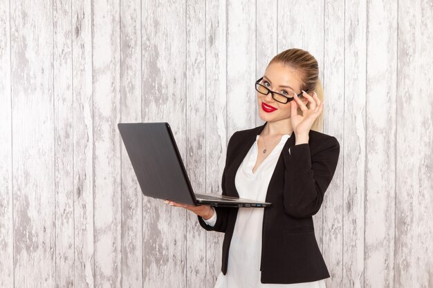 Vista frontal joven empresaria en ropa estricta chaqueta negra usando laptop en escritorio blanco trabajo trabajo oficina negocio