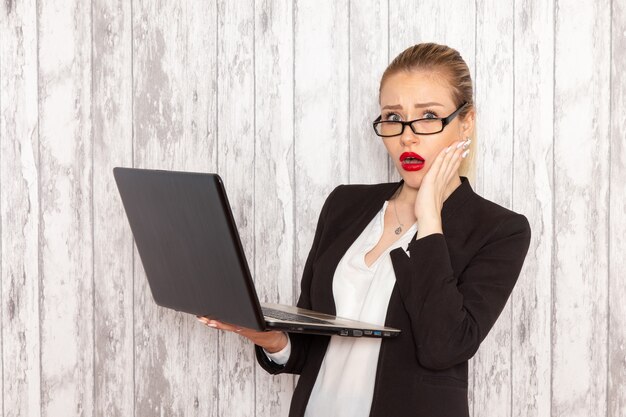 Vista frontal joven empresaria en ropa estricta chaqueta negra usando laptop en pared blanca trabajo trabajo oficina negocios trabajador femenino