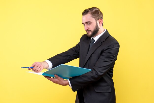 Vista frontal del joven empresario apuntando la pluma a un lado y sosteniendo la carpeta azul sobre amarillo