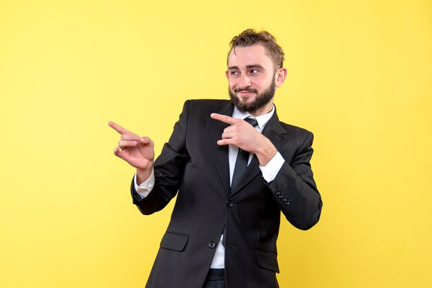 Vista frontal del joven empresario feliz señalando con el dedo a un lado en amarillo