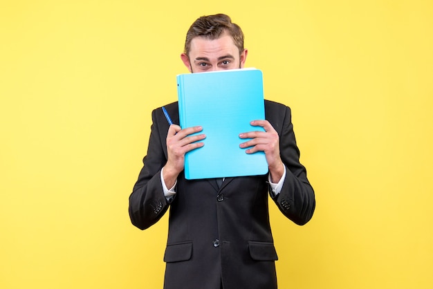 Vista frontal del joven empresario oculta la parte inferior de la cara con la carpeta azul sobre amarillo