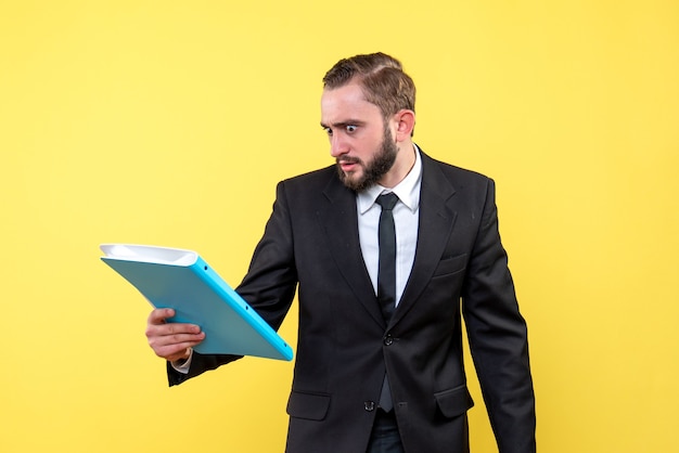 Vista frontal del joven empresario parece indignado enojado mientras revisa la carpeta azul sobre amarillo