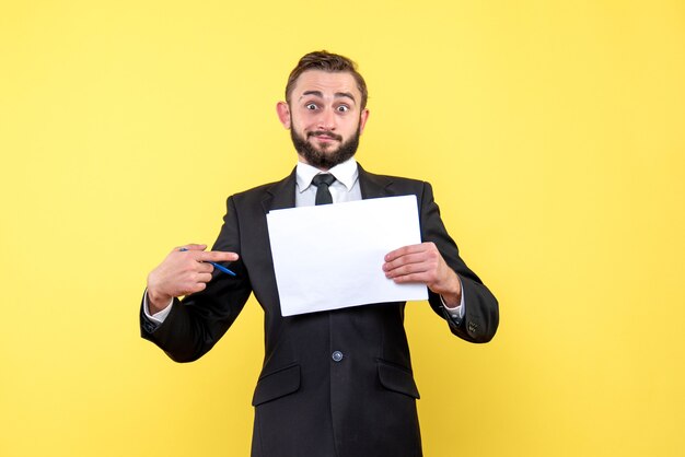 Vista frontal del joven empresario parece sorprendido y apunta con su dedo índice a un papel en blanco sobre amarillo