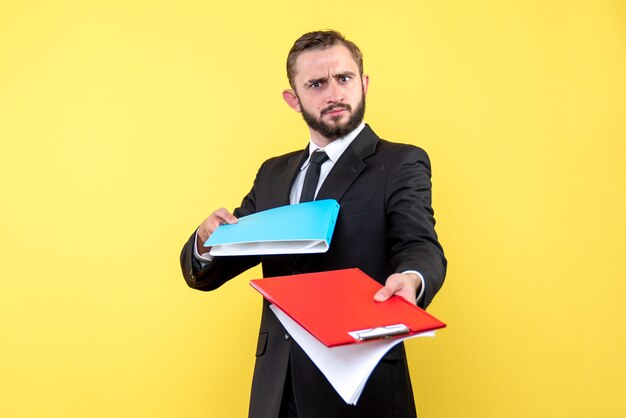 Vista frontal del joven empresario pasando con incertidumbre la carpeta azul y el portapapeles rojo sobre amarillo