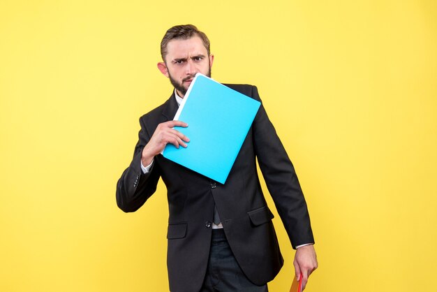 Vista frontal del joven empresario reflexivo toca su cara inferior con carpeta azul sobre amarillo