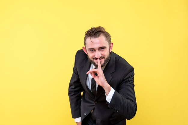 Vista frontal del joven empresario sonriente apuntando con el dedo a la boca en amarillo