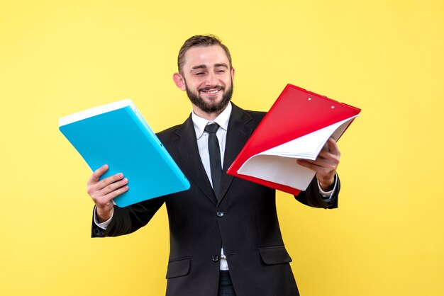 Vista frontal del joven empresario sonriente parece satisfecho mientras revisa el portapapeles rojo y sostiene la carpeta azul en amarillo