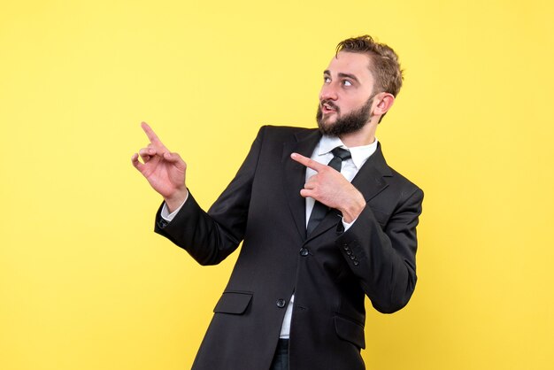 Vista frontal del joven empresario sorprendentemente señalando con el dedo a un lado en amarillo