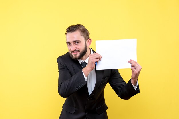 Vista frontal del joven empresario en un traje sonriendo y mantiene el papel en blanco a un lado a la izquierda en amarillo