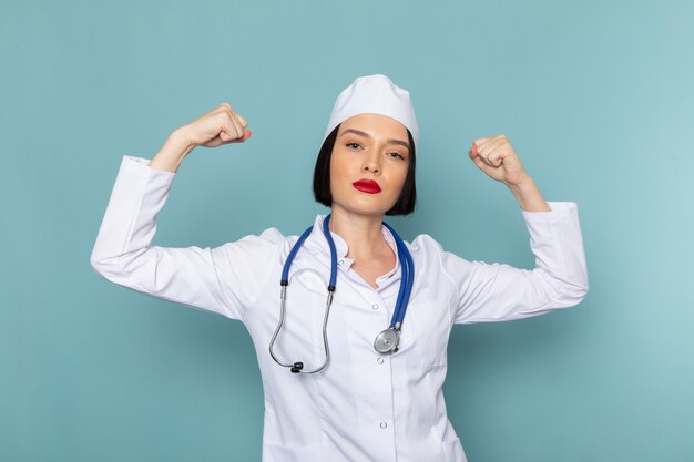 Una vista frontal joven enfermera en traje médico blanco y azul estetoscopio flexionando