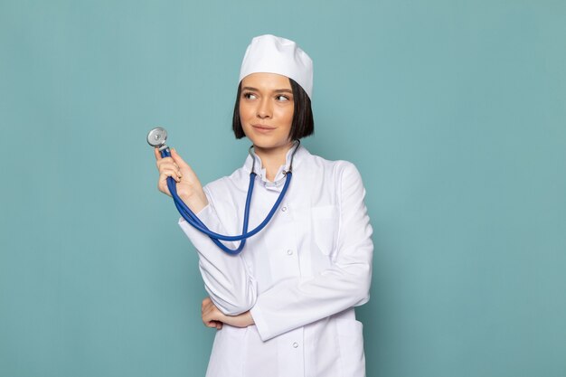 Una vista frontal joven enfermera en traje médico blanco y estetoscopio azul con expresión de pensamiento en el escritorio azul médico médico del hospital