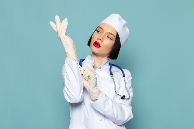 Una vista frontal joven enfermera en traje médico blanco y estetoscopio azul con guantes blancos en el escritorio azul médico médico del hospital