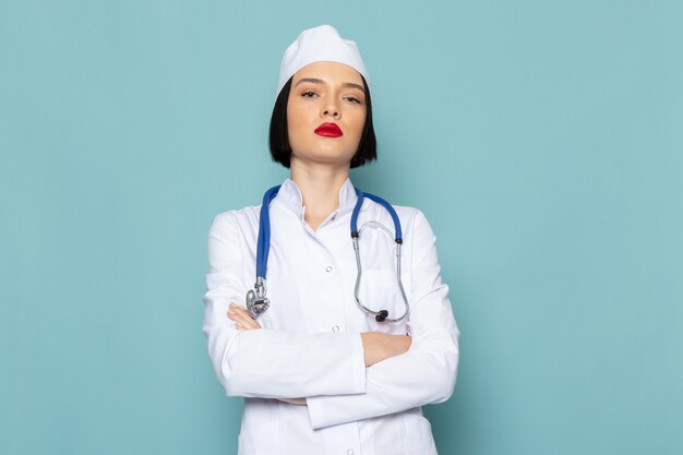 Una vista frontal joven enfermera en traje médico blanco y estetoscopio azul posando en el escritorio azul médico médico del hospital