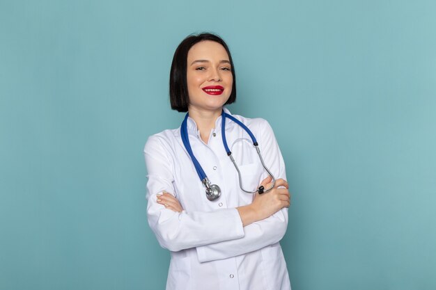 Una vista frontal joven enfermera en traje médico blanco y estetoscopio azul posando en el escritorio azul mujer médico del hospital de medicina