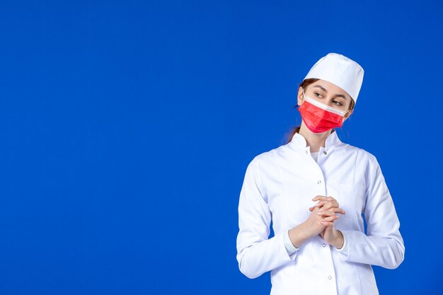 Vista frontal de la joven enfermera en traje médico con máscara roja sobre azul