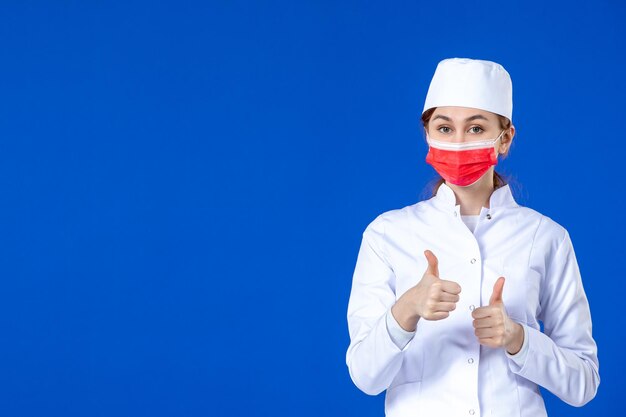 Vista frontal de la joven enfermera en traje médico con máscara roja sobre azul