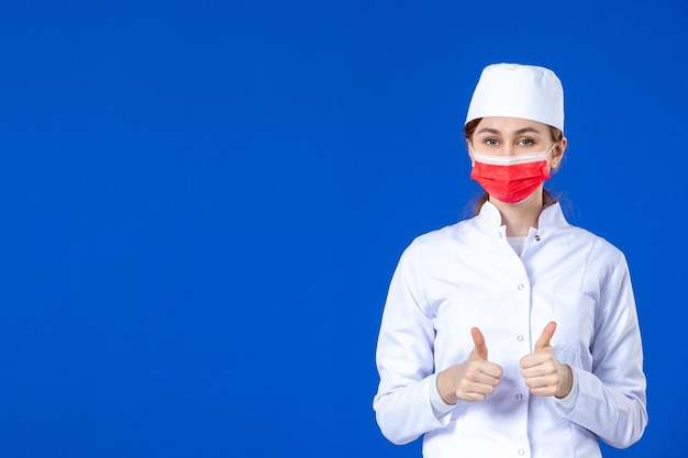 Vista frontal de la joven enfermera en traje médico con máscara roja sobre azul