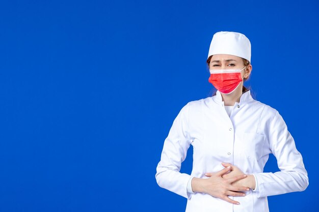 Vista frontal de la joven enfermera en traje médico con máscara roja sobre azul