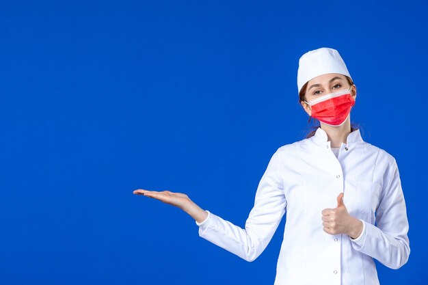 Vista frontal de la joven enfermera en traje médico con máscara roja sobre azul