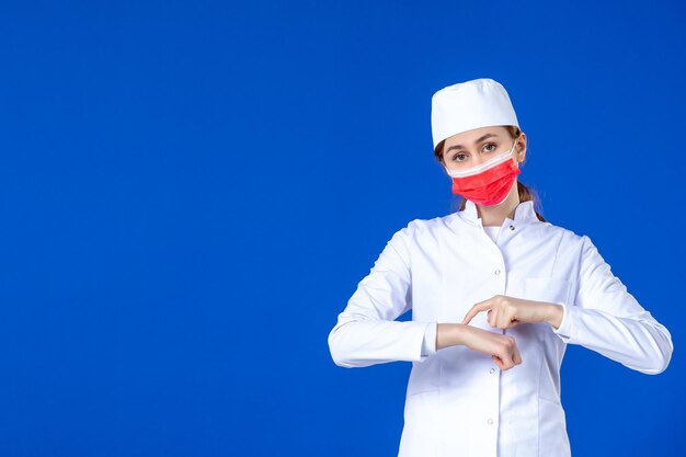 Vista frontal de la joven enfermera en traje médico con máscara roja sobre azul