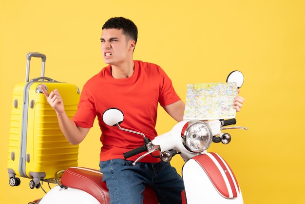 Vista frontal joven enojado en ropa casual en ciclomotor con mapa de viaje