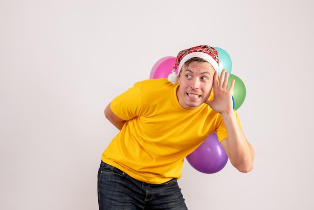 Vista frontal del joven escondiendo globos de colores en la pared blanca