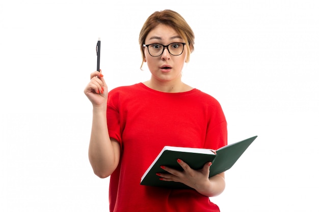 Una vista frontal joven estudiante en camiseta roja con cuaderno escribiendo notas idea sobre el blanco