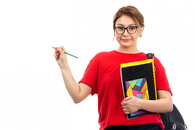 Una vista frontal joven estudiante en camiseta roja jeans negros con diferentes cuadernos y archivos con lápiz con bolsa en el blanco