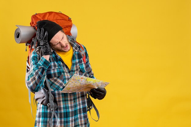 Vista frontal del joven excursionista confundido con guantes de cuero y mochila con mapa