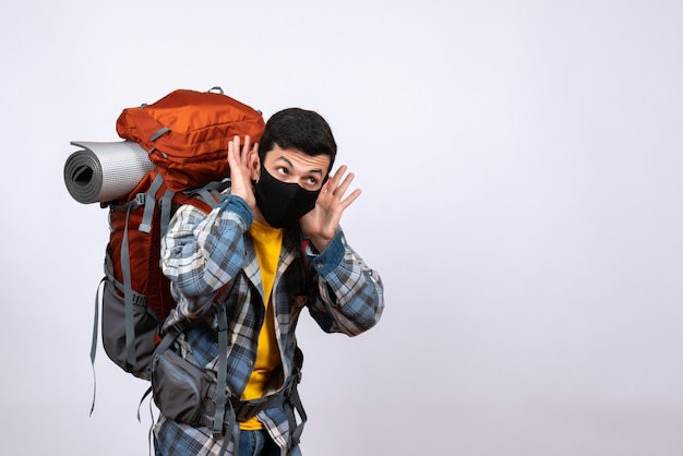 Vista frontal joven excursionista con mochila y máscara escuchando algo